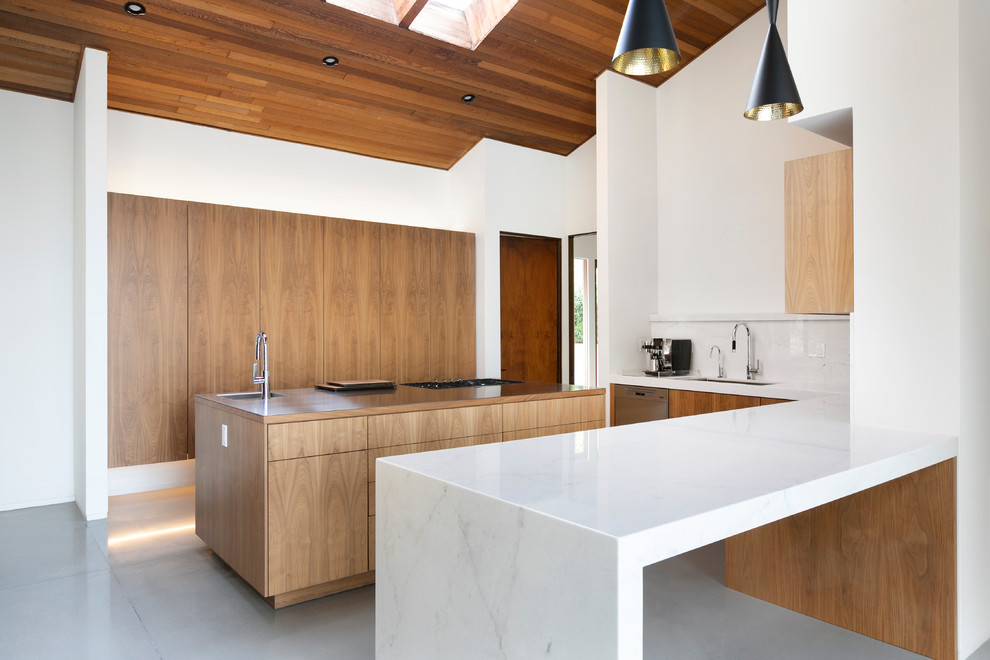 Cette photo montre une cuisine moderne en U et bois brun avec un évier encastré, un placard à porte plane, une crédence blanche, un électroménager en acier inoxydable, sol en béton ciré, îlot, un sol gris et un plan de travail blanc.
