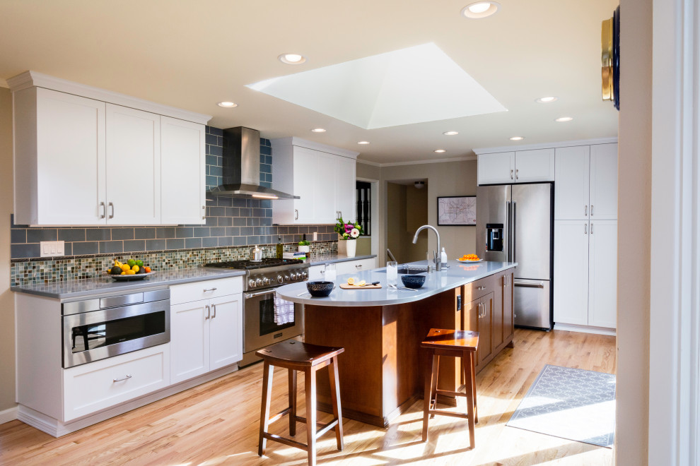 Design ideas for a traditional l-shaped kitchen in Seattle with a submerged sink, shaker cabinets, white cabinets, grey splashback, stainless steel appliances, medium hardwood flooring, an island, brown floors and white worktops.