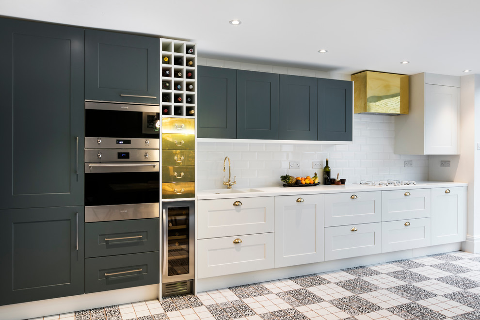 ロンドンにあるコンテンポラリースタイルのおしゃれなダイニングキッチン (ドロップインシンク、白いキャビネット、白いキッチンパネル、セラミックタイルのキッチンパネル、白い調理設備) の写真