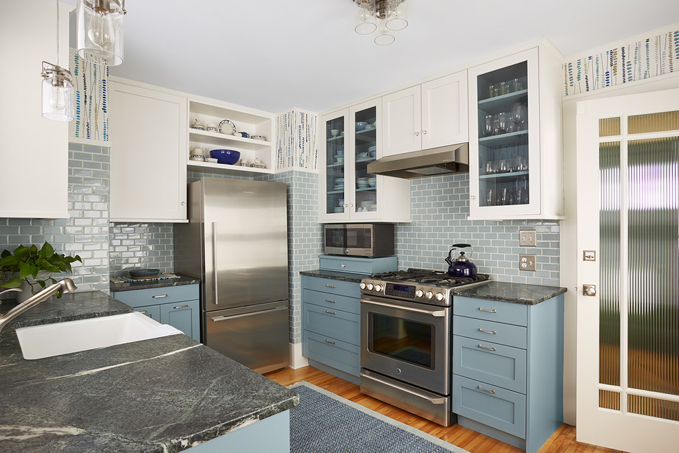 Enclosed kitchen - transitional u-shaped medium tone wood floor and brown floor enclosed kitchen idea in Minneapolis with a farmhouse sink, shaker cabinets, blue cabinets, soapstone countertops, blue backsplash, subway tile backsplash, stainless steel appliances and a peninsula