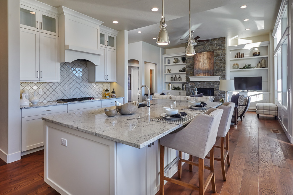 Inspiration for a transitional medium tone wood floor open concept kitchen remodel in Boise with an undermount sink, shaker cabinets, white cabinets, granite countertops, white backsplash, ceramic backsplash, stainless steel appliances and an island