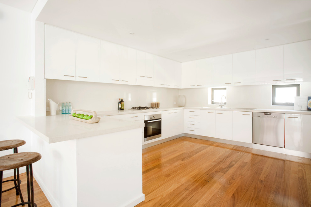 Große, Offene Moderne Küche in U-Form mit Triple-Waschtisch, Küchenrückwand in Beige, braunem Holzboden, flächenbündigen Schrankfronten, weißen Schränken, Küchengeräten aus Edelstahl und Halbinsel in Sydney