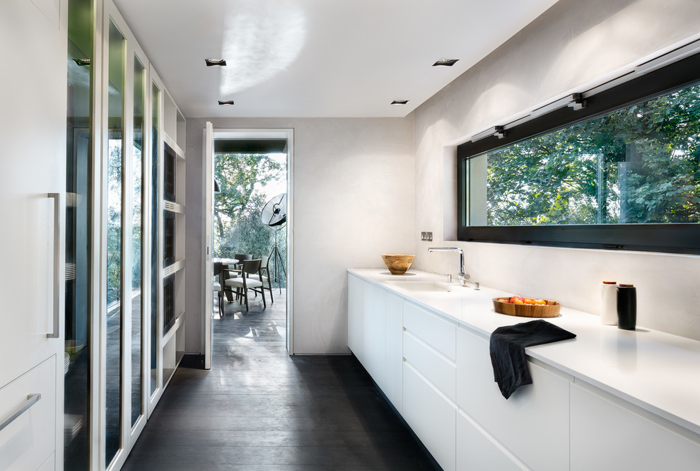 Moderne Wohnküche ohne Insel mit Unterbauwaschbecken, flächenbündigen Schrankfronten, weißen Schränken und dunklem Holzboden in London