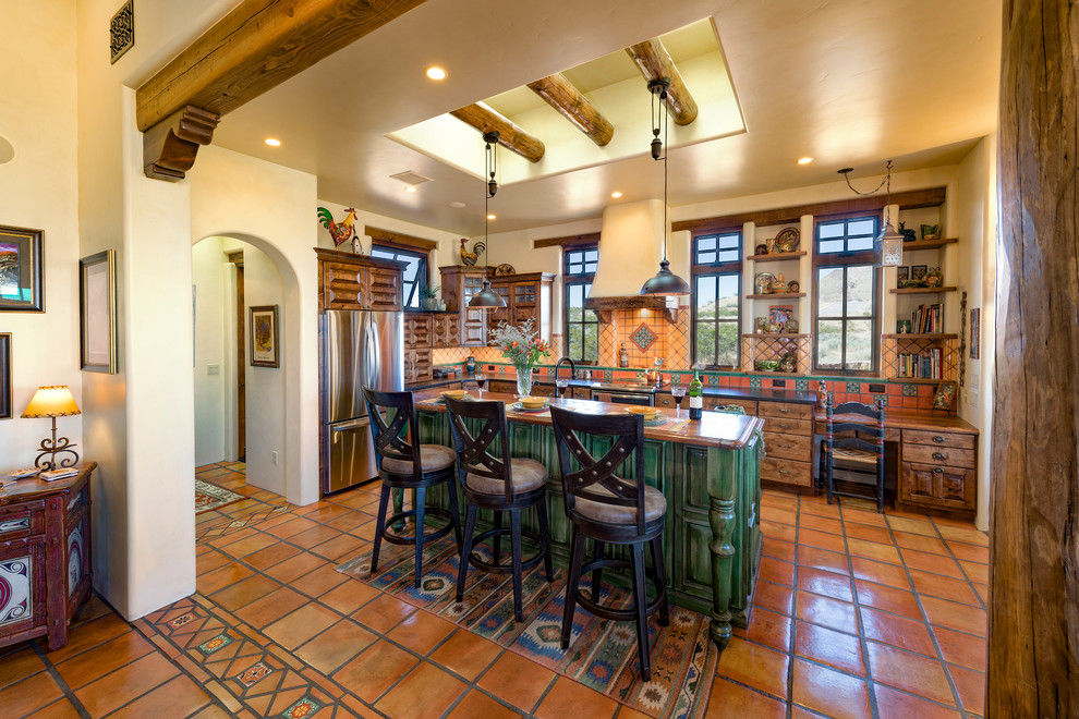 Mediterrane Küche in L-Form mit profilierten Schrankfronten, dunklen Holzschränken, bunter Rückwand, Küchengeräten aus Edelstahl, Kücheninsel und orangem Boden in Albuquerque