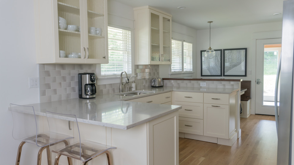 Example of a mid-sized eclectic u-shaped medium tone wood floor and yellow floor kitchen design in Indianapolis with an undermount sink, glass-front cabinets, white cabinets, gray backsplash, subway tile backsplash, stainless steel appliances, an island and gray countertops