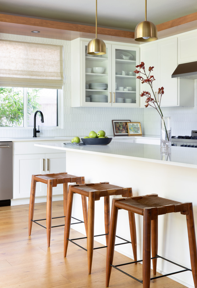 Mittelgroße Moderne Küche in L-Form mit Unterbauwaschbecken, Schrankfronten im Shaker-Stil, weißen Schränken, Küchenrückwand in Weiß, Küchengeräten aus Edelstahl, braunem Holzboden, Kücheninsel, braunem Boden und weißer Arbeitsplatte in Austin