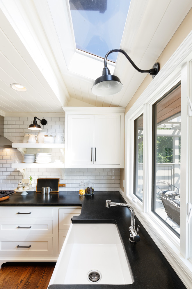 Inspiration for a mid-sized cottage l-shaped medium tone wood floor and brown floor eat-in kitchen remodel in Cincinnati with a farmhouse sink, white backsplash, subway tile backsplash, paneled appliances, an island, raised-panel cabinets, white cabinets and granite countertops