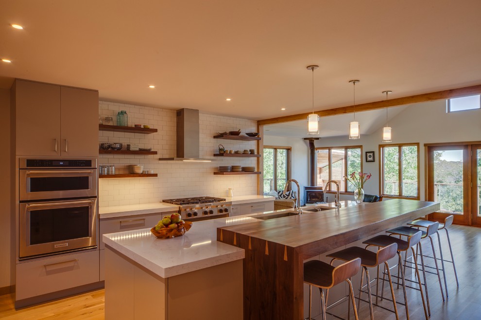 Design ideas for a large contemporary kitchen in Other with an island, a submerged sink, flat-panel cabinets, grey cabinets, engineered stone countertops, white splashback, metro tiled splashback, stainless steel appliances and medium hardwood flooring.