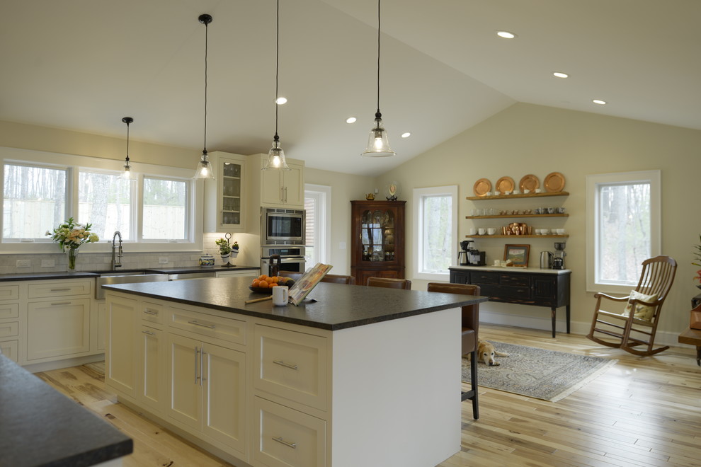 Inspiration for a large transitional l-shaped light wood floor open concept kitchen remodel in DC Metro with a farmhouse sink, shaker cabinets, white cabinets, granite countertops, white backsplash, stone tile backsplash, stainless steel appliances and an island