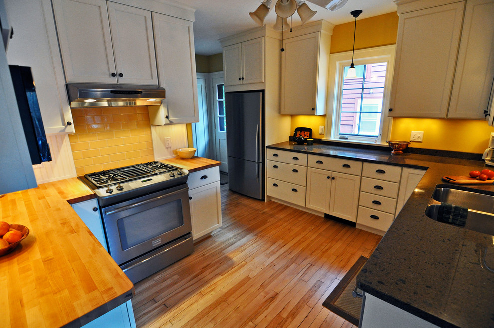 Klassische Küche mit Granit-Arbeitsplatte, weißen Schränken, Rückwand aus Keramikfliesen und Küchengeräten aus Edelstahl in Sonstige