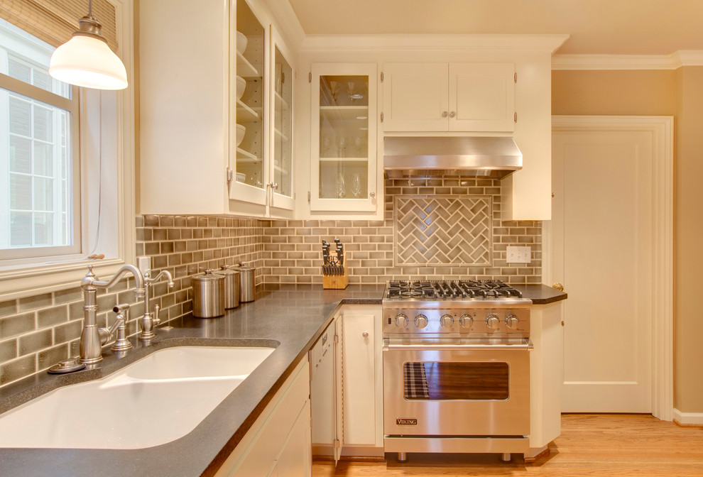 This is an example of a traditional kitchen in Seattle with a double-bowl sink, glass-front cabinets, beige splashback, metro tiled splashback, stainless steel appliances and white cabinets.