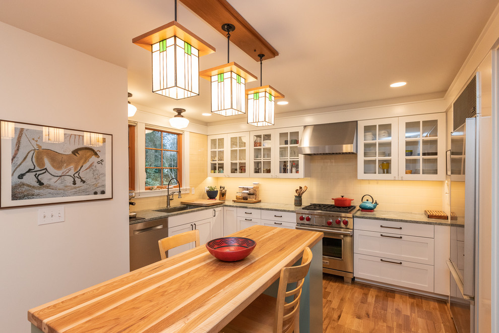 シアトルにあるトラディショナルスタイルのおしゃれなキッチン (アンダーカウンターシンク、シェーカースタイル扉のキャビネット、白いキャビネット、ベージュキッチンパネル、シルバーの調理設備、無垢フローリング、茶色い床、グレーのキッチンカウンター) の写真