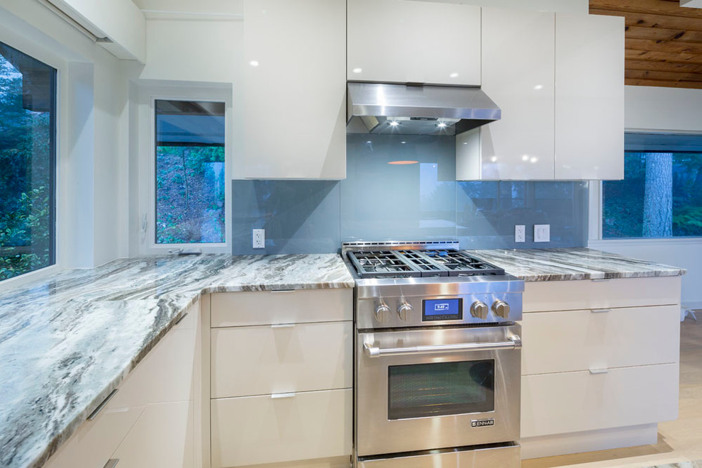 Eat-in kitchen - mid-sized modern u-shaped light wood floor and beige floor eat-in kitchen idea in Vancouver with an undermount sink, flat-panel cabinets, white cabinets, blue backsplash, glass sheet backsplash, stainless steel appliances, an island and marble countertops