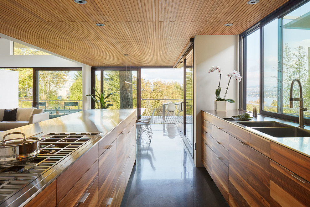 На фото: параллельная кухня-гостиная в современном стиле с фасадами цвета дерева среднего тона, столешницей из нержавеющей стали, островом, двойной мойкой, плоскими фасадами и окном
