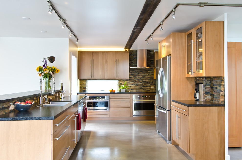 Example of a large minimalist galley concrete floor open concept kitchen design in Seattle with a double-bowl sink, flat-panel cabinets, light wood cabinets, multicolored backsplash, stone tile backsplash, stainless steel appliances and a peninsula