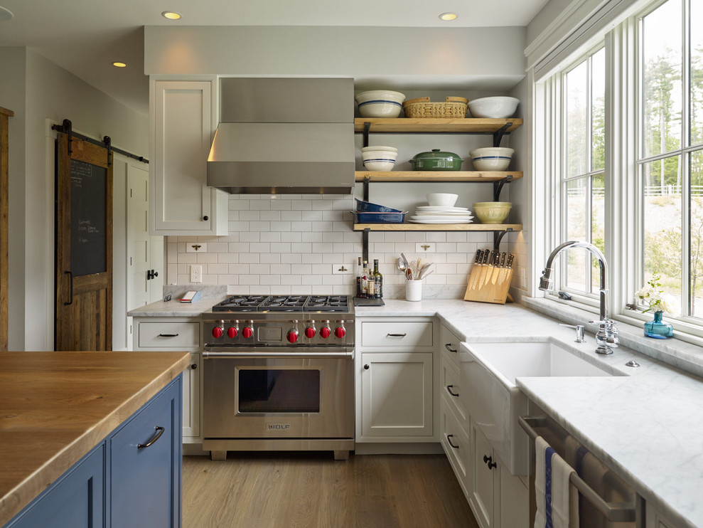 Large country u-shaped open plan kitchen in Portland Maine with recessed-panel cabinets, blue cabinets, marble worktops, white splashback, metro tiled splashback, stainless steel appliances and an island.