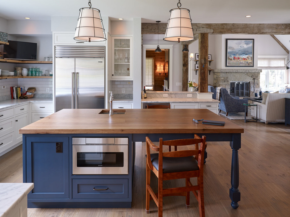 Photo of a large country u-shaped open plan kitchen in Portland Maine with recessed-panel cabinets, blue cabinets, marble worktops, white splashback, metro tiled splashback, stainless steel appliances, an island, a submerged sink, medium hardwood flooring, brown floors and white worktops.