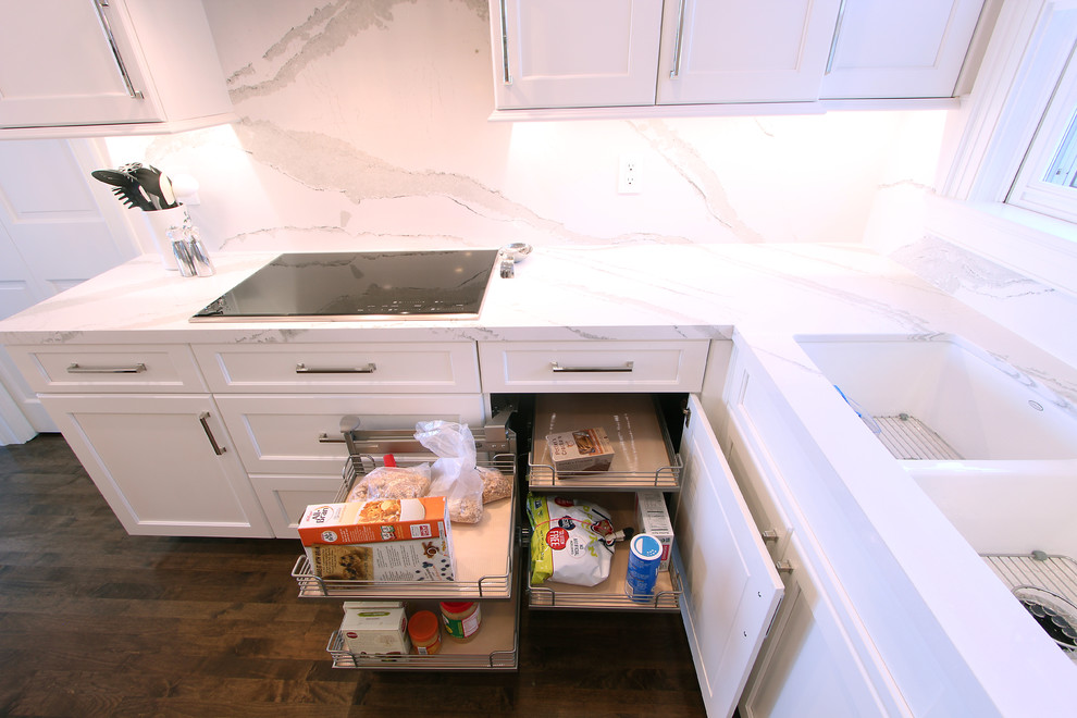 Foto på ett litet vintage vit kök, med en undermonterad diskho, luckor med infälld panel, vita skåp, bänkskiva i kvarts, vitt stänkskydd, stänkskydd i sten, integrerade vitvaror, mörkt trägolv, en köksö och brunt golv
