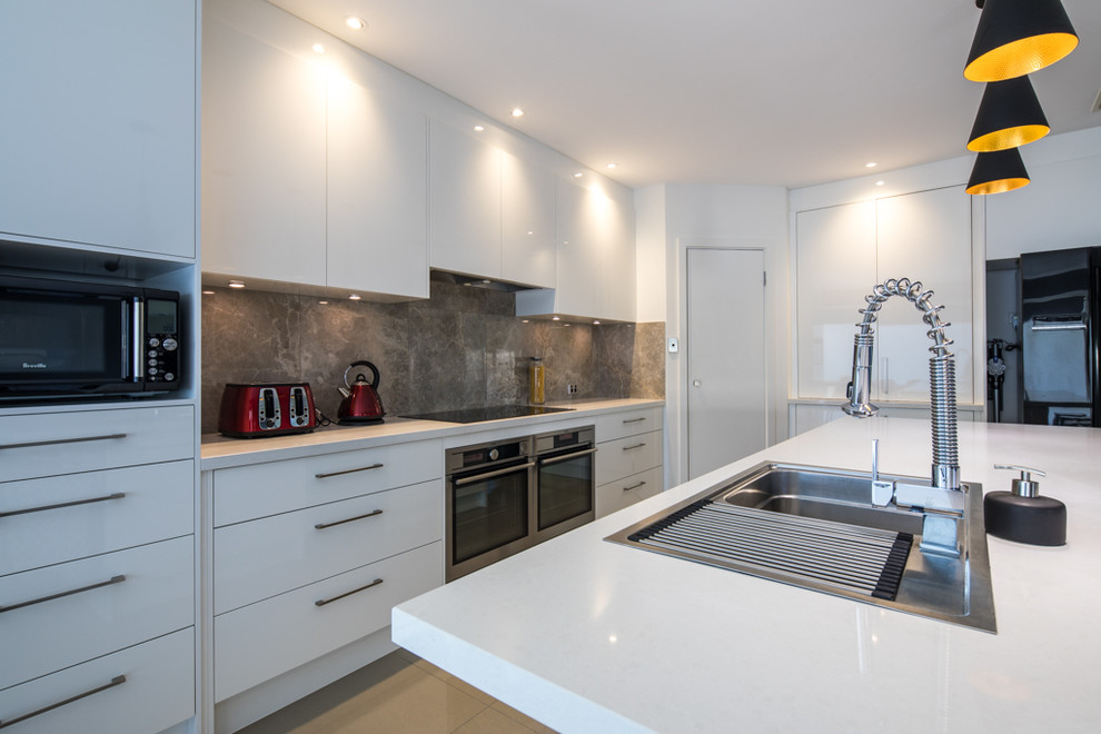This is an example of a large contemporary galley kitchen pantry in Adelaide with a single-bowl sink, recessed-panel cabinets, white cabinets, engineered stone countertops, brown splashback, terracotta splashback, stainless steel appliances, terracotta flooring, an island and beige floors.