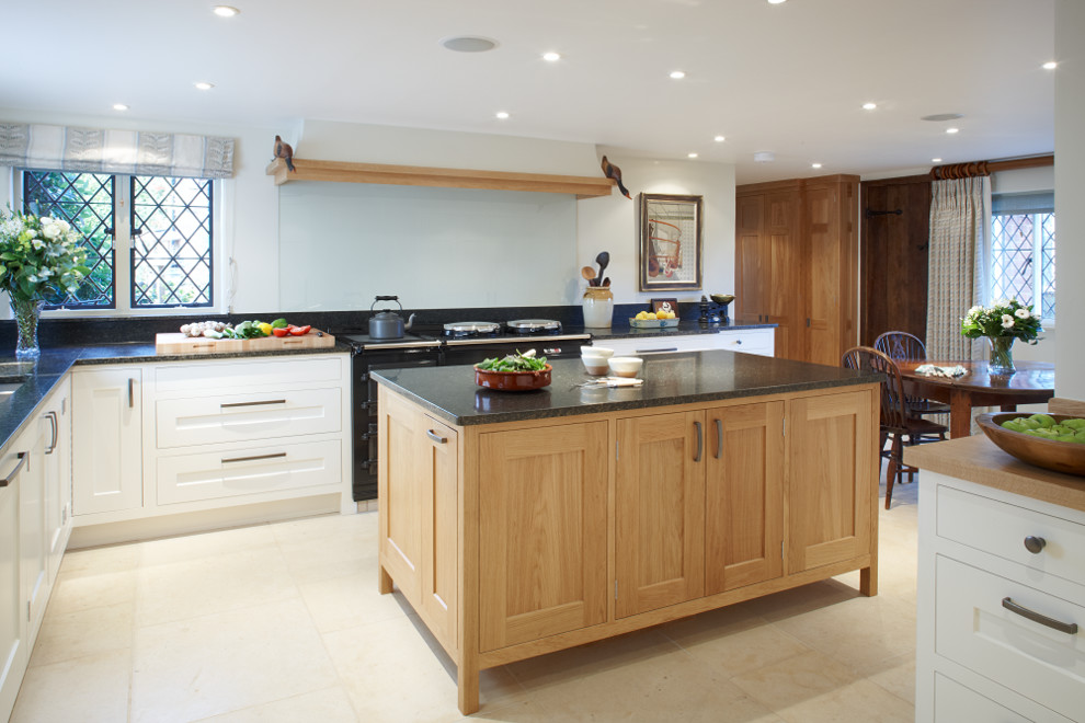 This is an example of a large modern l-shaped kitchen/diner in Surrey with a double-bowl sink, shaker cabinets, light wood cabinets, granite worktops, black splashback, stone slab splashback, stainless steel appliances, limestone flooring and an island.