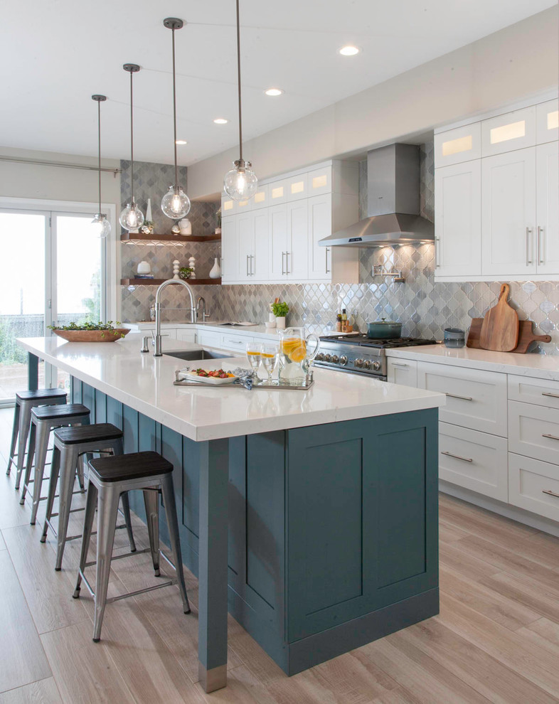 Large classic kitchen in San Diego with a submerged sink, white cabinets, grey splashback, stainless steel appliances, light hardwood flooring, an island, beige floors, white worktops, engineered stone countertops, glass tiled splashback and shaker cabinets.