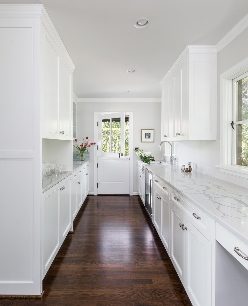 Design ideas for a large traditional kitchen pantry in Seattle with a submerged sink, recessed-panel cabinets, white cabinets, engineered stone countertops, blue splashback, glass tiled splashback, stainless steel appliances, medium hardwood flooring, an island and brown floors.