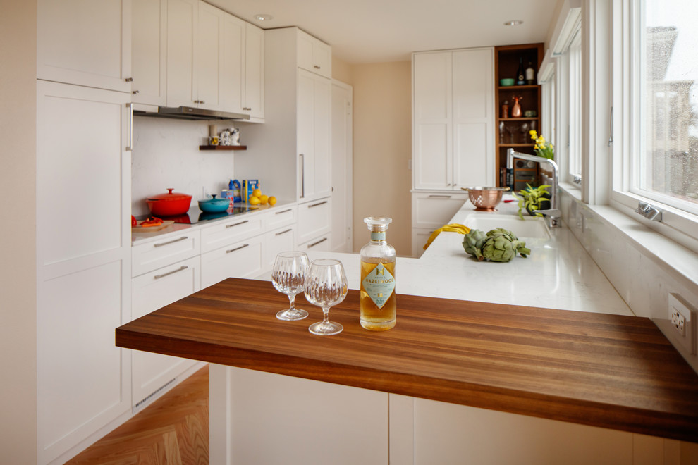 Klassisk inredning av ett litet kök, med en undermonterad diskho, skåp i shakerstil, vita skåp, bänkskiva i kvarts, vitt stänkskydd, rostfria vitvaror, ljust trägolv och en halv köksö