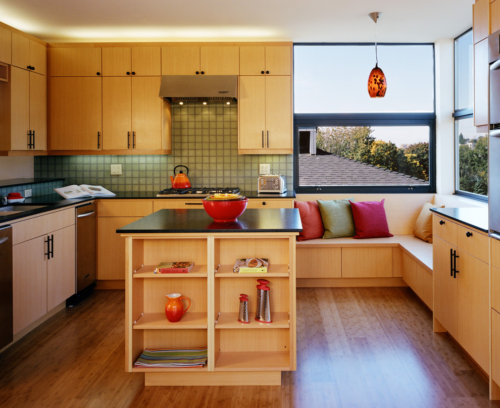Свежая идея для дизайна: угловая кухня в современном стиле с плоскими фасадами, светлыми деревянными фасадами и зеленым фартуком - отличное фото интерьера