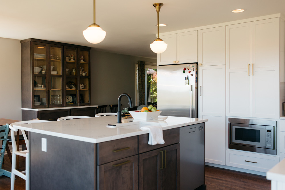 Photo of a large contemporary l-shaped kitchen/diner in Seattle with a submerged sink, shaker cabinets, white cabinets, composite countertops, white splashback, mosaic tiled splashback, stainless steel appliances, dark hardwood flooring, an island and brown floors.