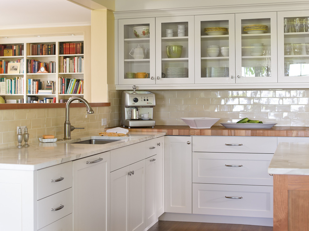Modelo de cocina clásica con fregadero bajoencimera, armarios estilo shaker, puertas de armario blancas, encimera de madera, salpicadero beige y salpicadero de azulejos tipo metro