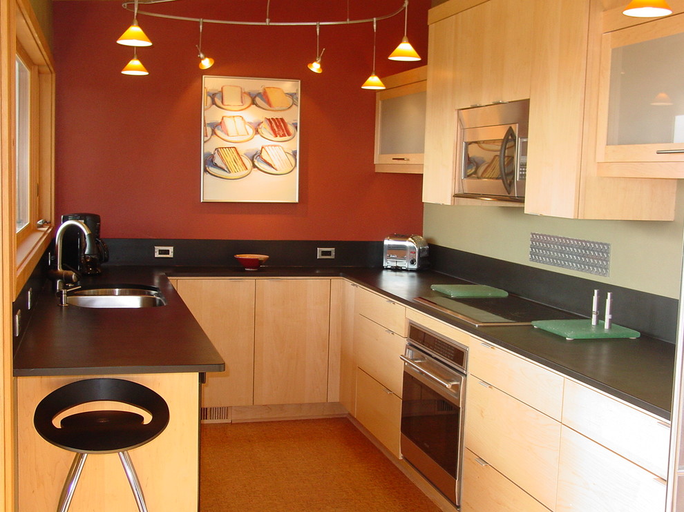 На фото: отдельная, п-образная кухня в стиле модернизм с двойной мойкой, плоскими фасадами, светлыми деревянными фасадами, черным фартуком и техникой из нержавеющей стали