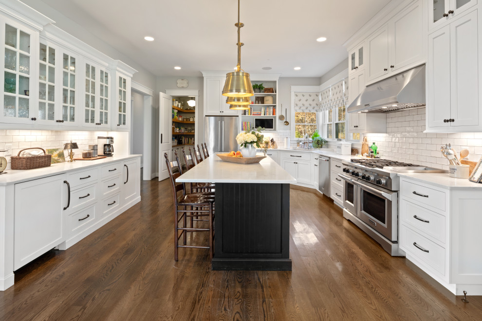 This is an example of an expansive rural u-shaped kitchen in Cincinnati with a submerged sink, shaker cabinets, white cabinets, white splashback, metro tiled splashback, stainless steel appliances, medium hardwood flooring, an island, brown floors and white worktops.