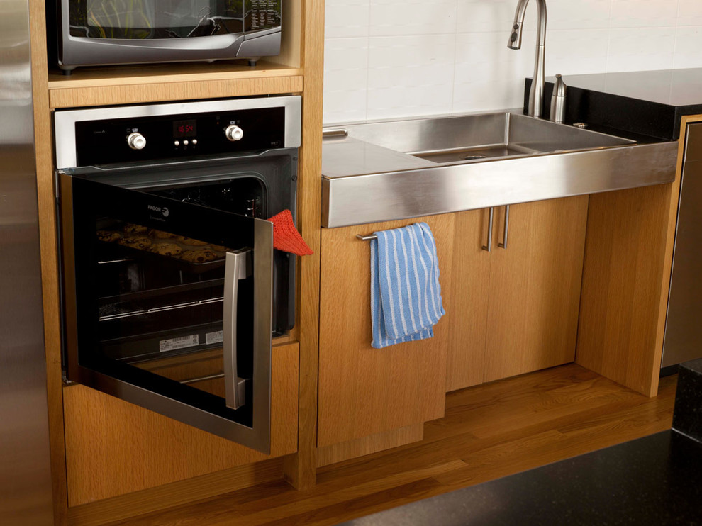 Example of a 1950s galley medium tone wood floor eat-in kitchen design in Seattle with a single-bowl sink, flat-panel cabinets, medium tone wood cabinets, granite countertops, white backsplash, ceramic backsplash, stainless steel appliances and an island