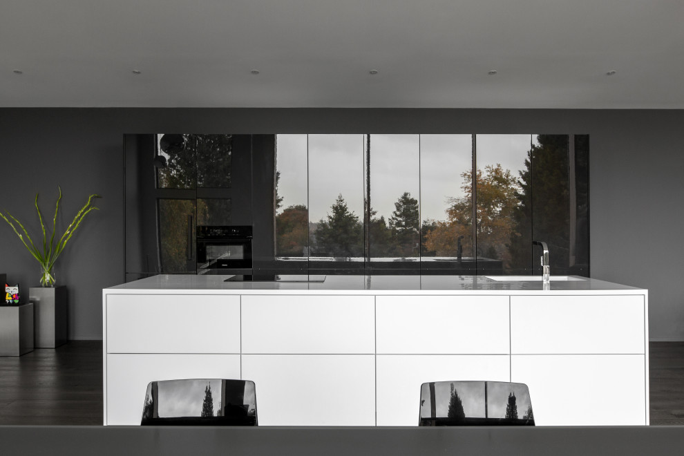 This is an example of a modern kitchen/diner in Seattle with an integrated sink, flat-panel cabinets, composite countertops, integrated appliances, medium hardwood flooring, an island and white worktops.