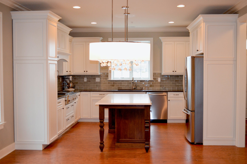 Small elegant u-shaped medium tone wood floor and brown floor eat-in kitchen photo in Philadelphia with an undermount sink, raised-panel cabinets, white cabinets, marble countertops, gray backsplash, stone tile backsplash, stainless steel appliances and an island