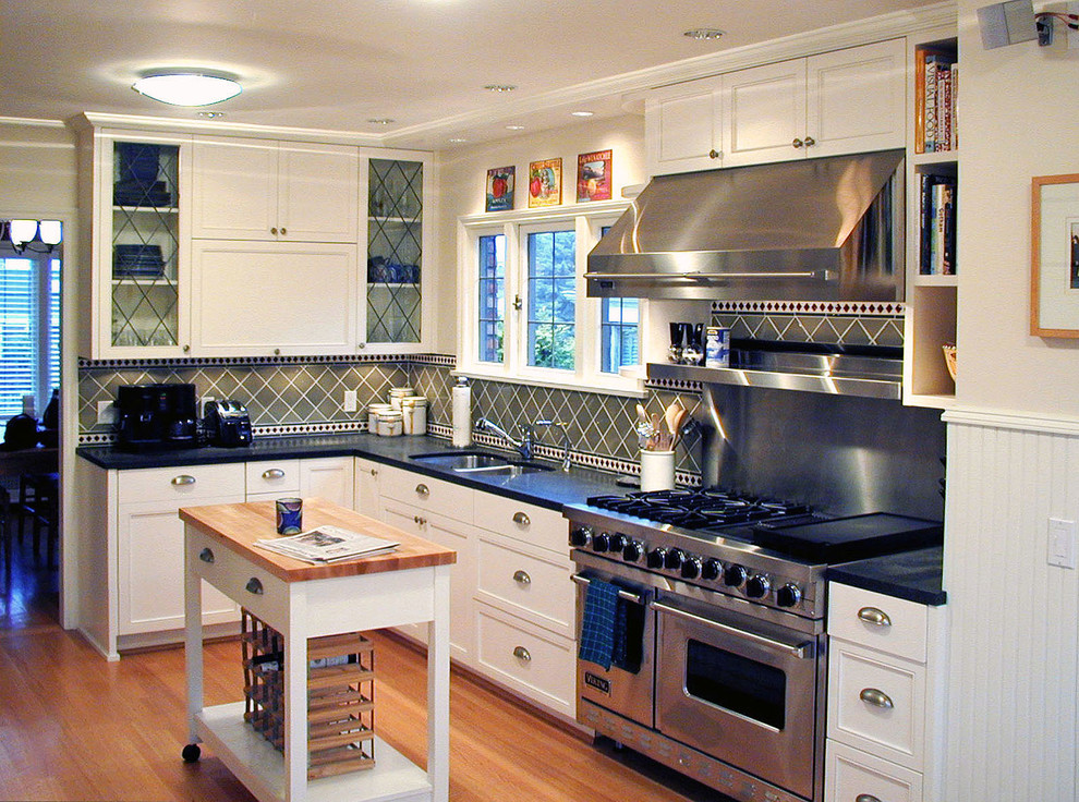 シアトルにあるトラディショナルスタイルのおしゃれなキッチン (ガラス扉のキャビネット、シルバーの調理設備、木材カウンター、ダブルシンク、白いキャビネット、緑のキッチンパネル) の写真