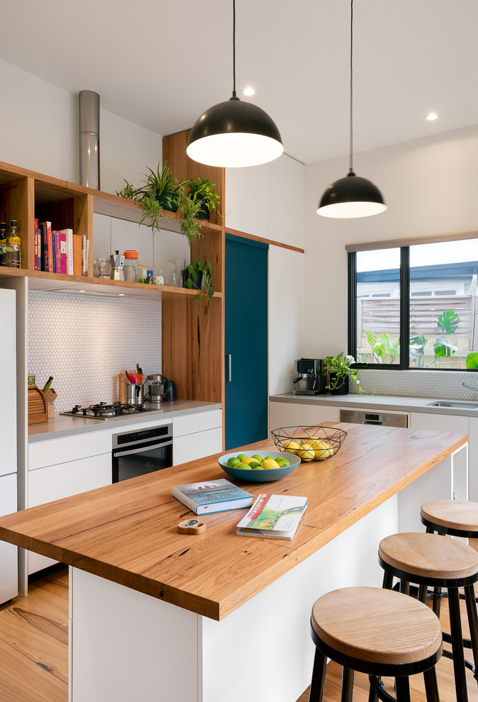 Foto på ett mellanstort funkis grå linjärt kök, med en undermonterad diskho, släta luckor, vita skåp, träbänkskiva, vitt stänkskydd, stänkskydd i mosaik, rostfria vitvaror, mellanmörkt trägolv och en köksö