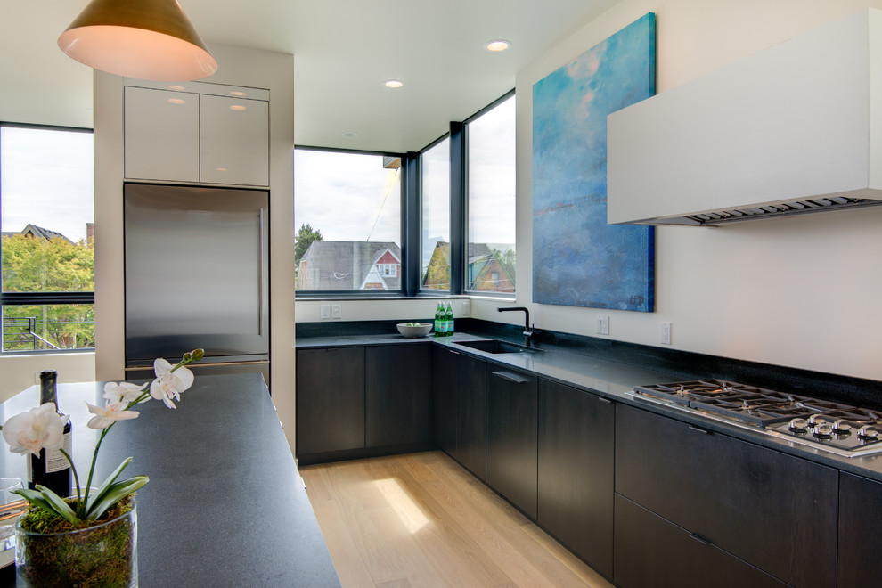 Moderne Küche in L-Form mit Unterbauwaschbecken, flächenbündigen Schrankfronten, dunklen Holzschränken, Quarzit-Arbeitsplatte, Küchenrückwand in Weiß, Küchengeräten aus Edelstahl, hellem Holzboden und Kücheninsel in Seattle