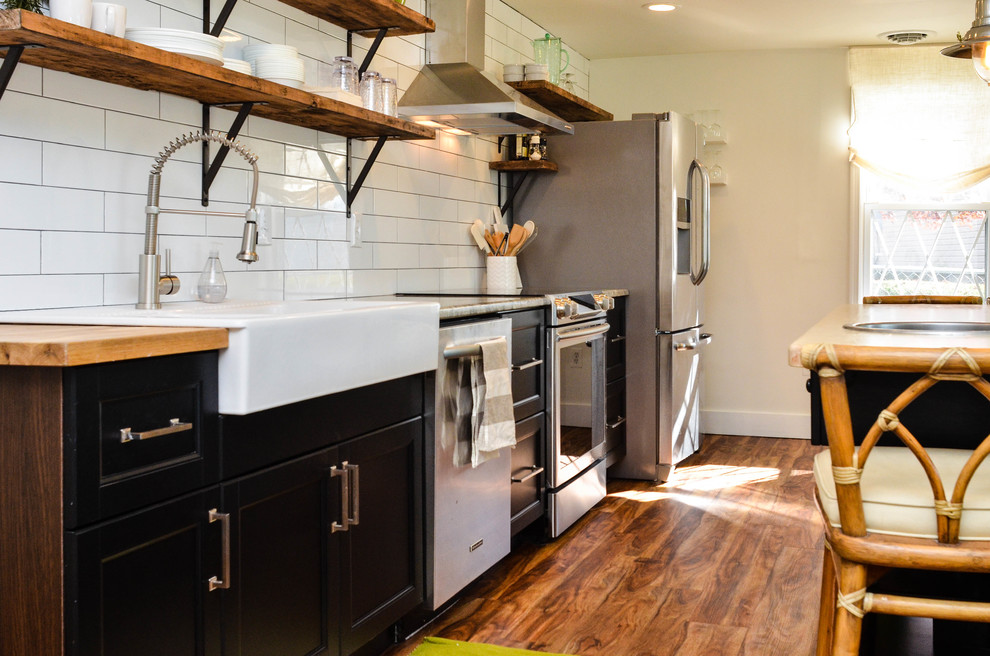 Inspiration for a mid-sized cottage medium tone wood floor open concept kitchen remodel in DC Metro with a farmhouse sink, recessed-panel cabinets, black cabinets, granite countertops, white backsplash, subway tile backsplash, stainless steel appliances and an island