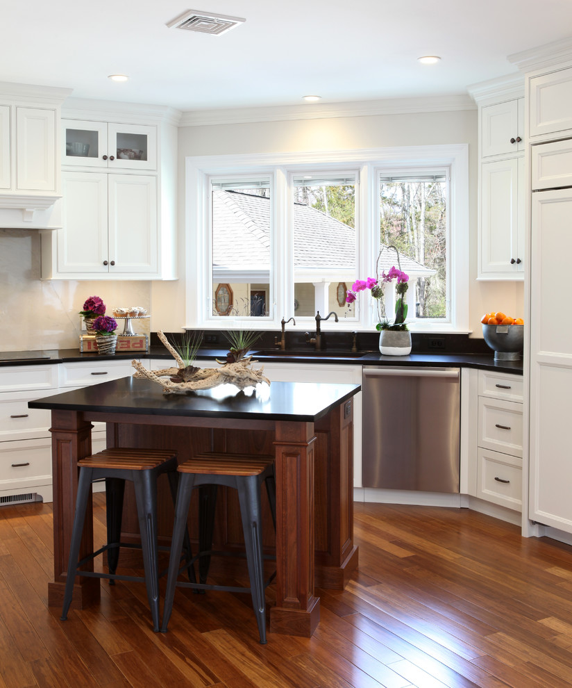 Inredning av ett klassiskt stort kök, med en undermonterad diskho, luckor med infälld panel, vita skåp, granitbänkskiva, vitt stänkskydd, stänkskydd i sten, rostfria vitvaror, mellanmörkt trägolv, en köksö och brunt golv