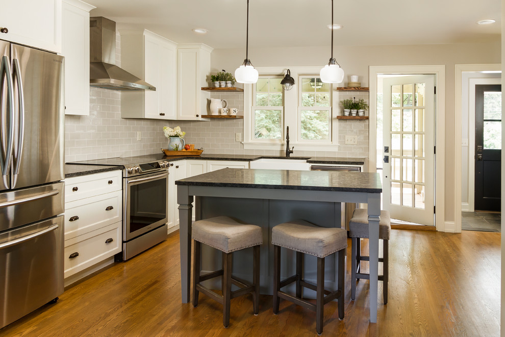 Klassisk inredning av ett litet kök, med en rustik diskho, skåp i shakerstil, vita skåp, granitbänkskiva, blått stänkskydd, stänkskydd i tunnelbanekakel, rostfria vitvaror, ljust trägolv, en köksö och brunt golv
