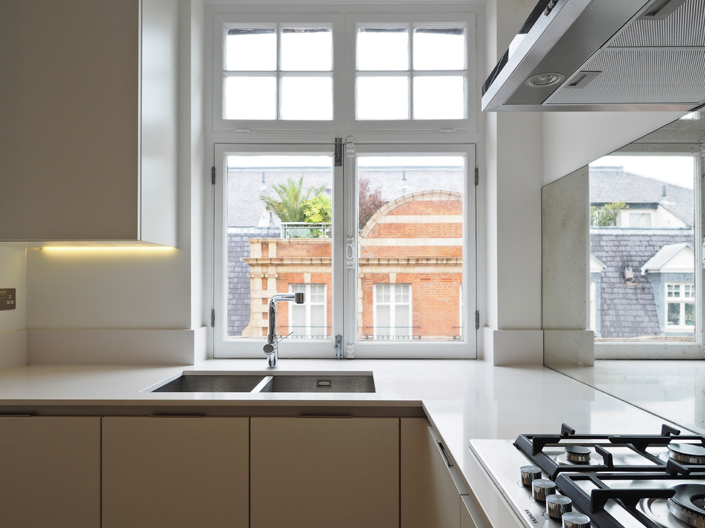 Immagine di una cucina minimal con lavello a doppia vasca, ante lisce, ante bianche, top in superficie solida, paraspruzzi a specchio, elettrodomestici in acciaio inossidabile e pavimento in pietra calcarea