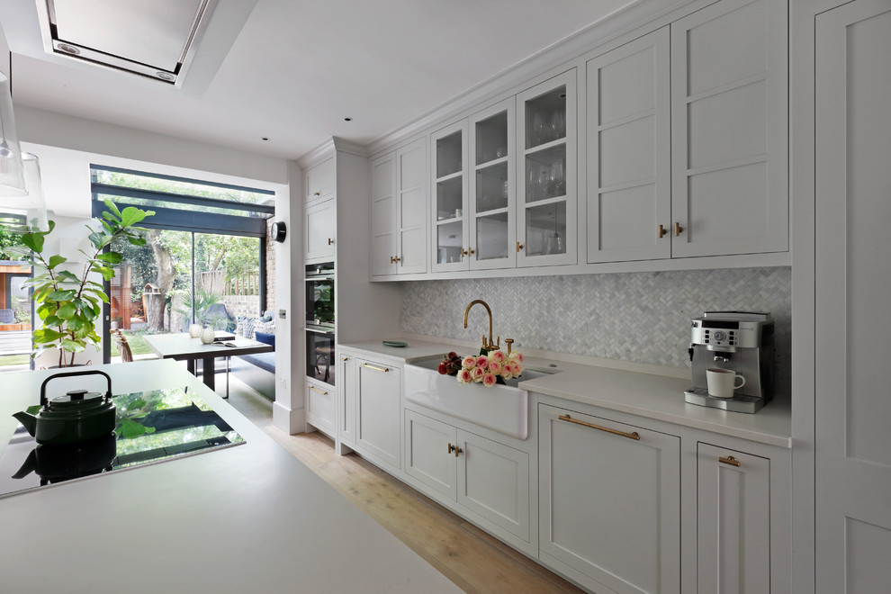 Large contemporary u-shaped kitchen/diner in London with a submerged sink, shaker cabinets, white cabinets, engineered stone countertops, stainless steel appliances, light hardwood flooring, an island and white worktops.