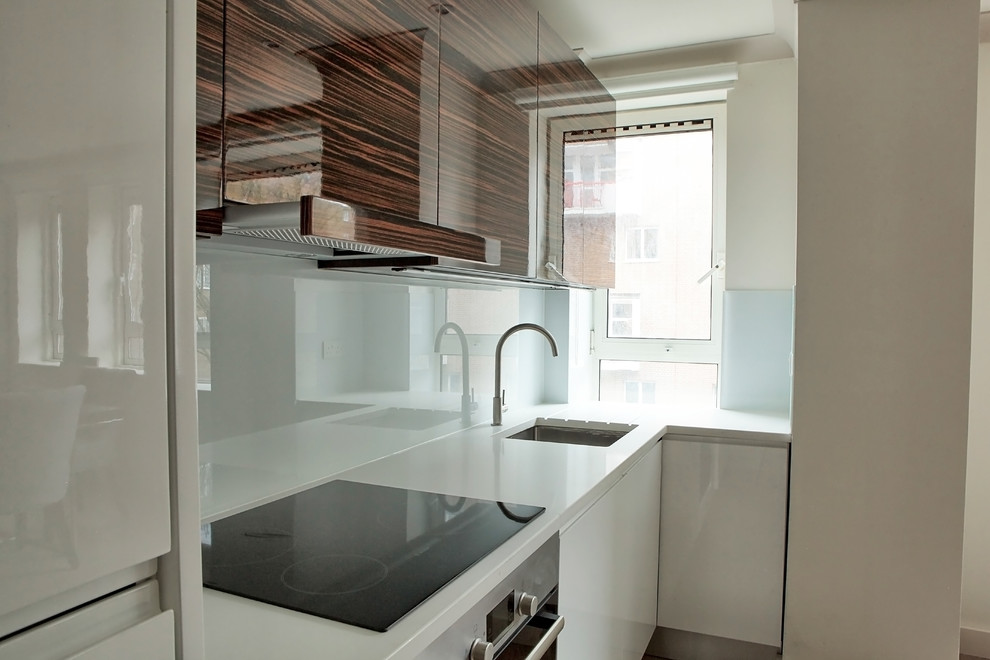 Bild på ett mellanstort funkis linjärt kök med öppen planlösning, med en undermonterad diskho, släta luckor, bänkskiva i kvarts, vitt stänkskydd och glaspanel som stänkskydd