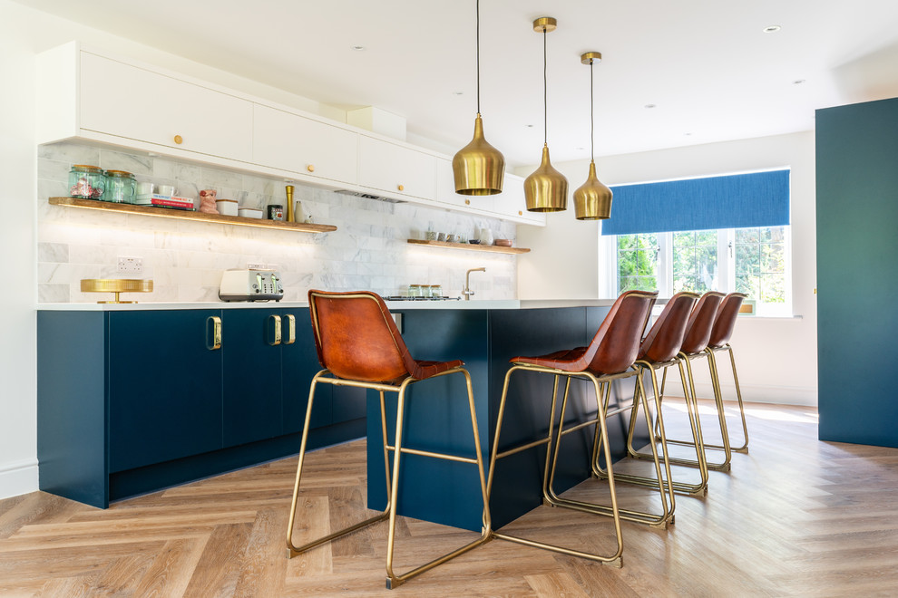 Cette image montre une cuisine design avec un placard à porte plane, des portes de placard bleues, une crédence grise, parquet clair, îlot, un sol marron et un plan de travail blanc.