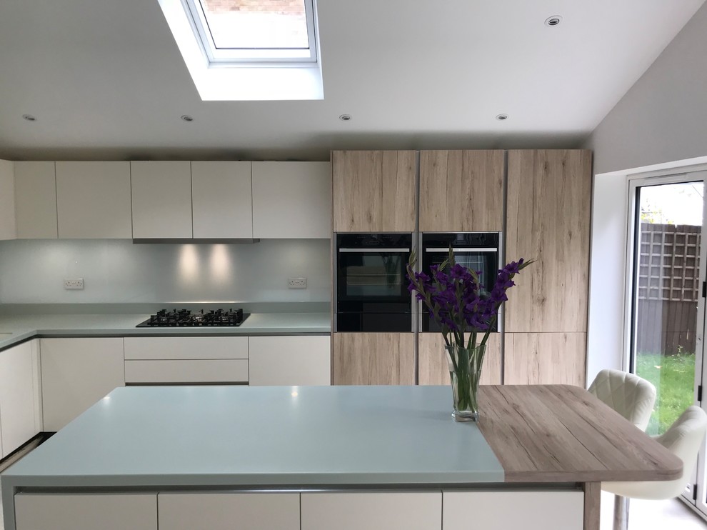 Inspiration for a medium sized modern l-shaped kitchen/diner in Kent with a submerged sink, flat-panel cabinets, white cabinets, composite countertops, white splashback, glass sheet splashback, black appliances, porcelain flooring, an island, grey floors and green worktops.