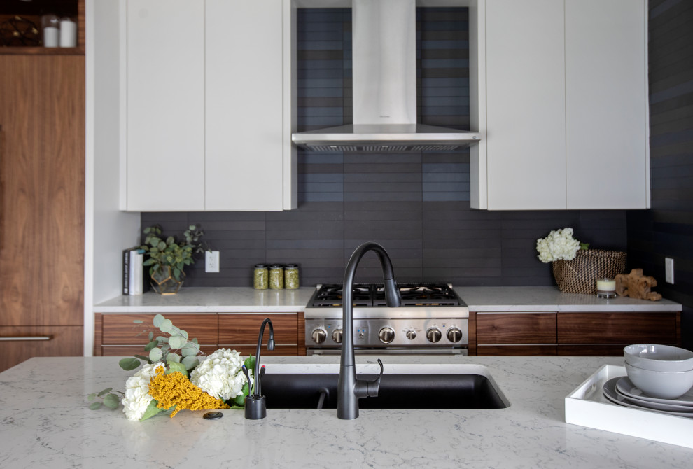 Foto på ett funkis vit linjärt kök och matrum, med en undermonterad diskho, släta luckor, bänkskiva i kvartsit, svart stänkskydd, stänkskydd i porslinskakel, rostfria vitvaror och en halv köksö