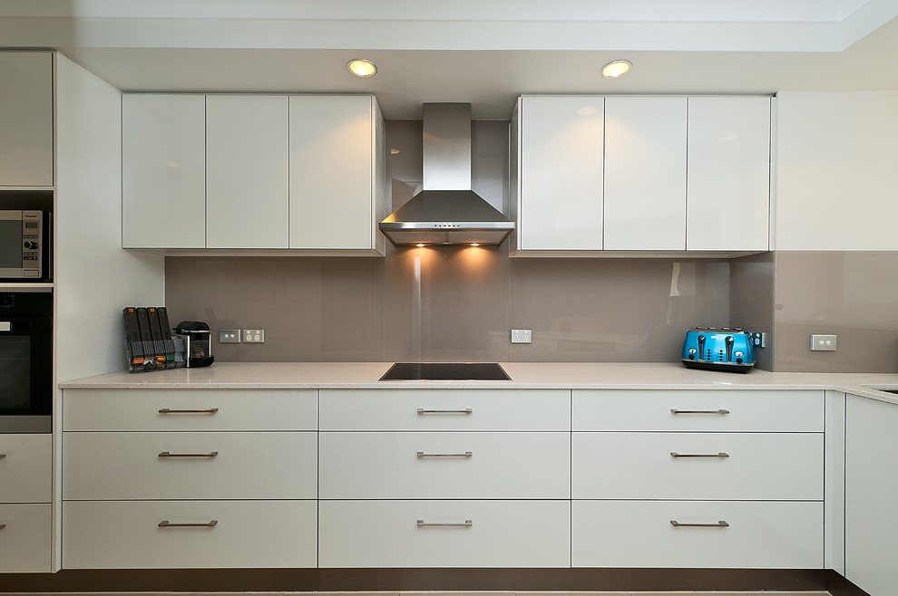 Small modern l-shaped enclosed kitchen in Gold Coast - Tweed with a submerged sink, flat-panel cabinets, white cabinets, engineered stone countertops, grey splashback, glass sheet splashback, stainless steel appliances and no island.