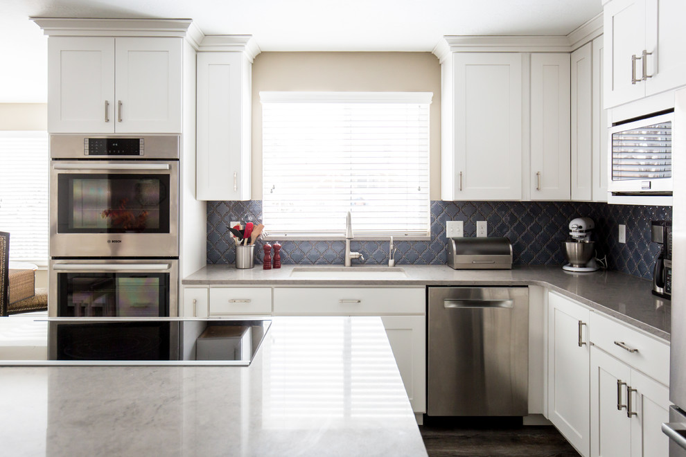 Exempel på ett mellanstort klassiskt grå grått kök, med en undermonterad diskho, skåp i shakerstil, vita skåp, bänkskiva i kvarts, blått stänkskydd, stänkskydd i mosaik, rostfria vitvaror, vinylgolv, en köksö och brunt golv