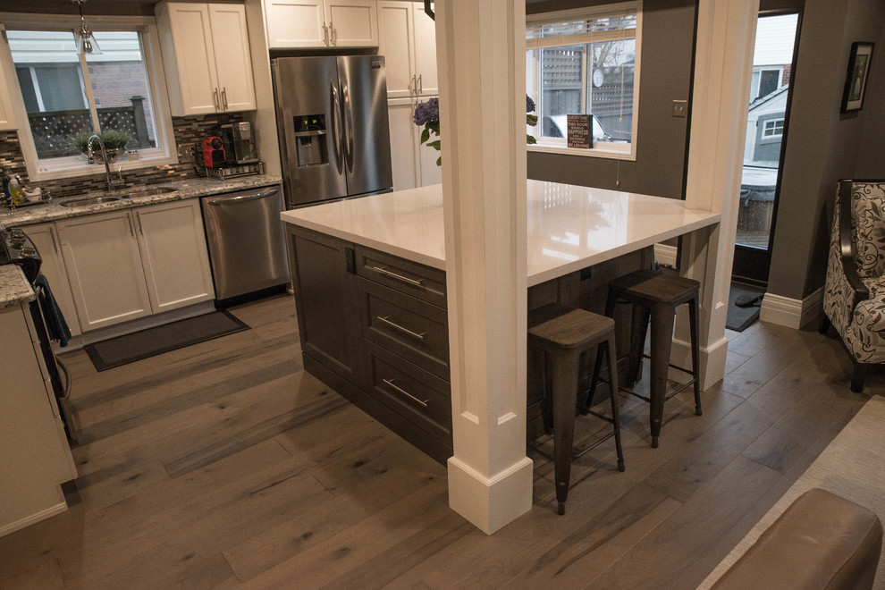 Klassisk inredning av ett mellanstort l-kök, med en undermonterad diskho, skåp i shakerstil, vita skåp, granitbänkskiva, flerfärgad stänkskydd, stänkskydd i stickkakel, rostfria vitvaror, mörkt trägolv, en köksö och brunt golv
